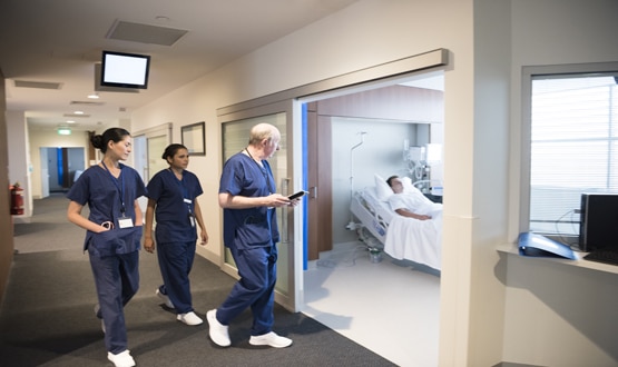 Nurses and doctor in hospital walking towards hospital room. Male patient recovering on hospital ward with medical professionals arriving.