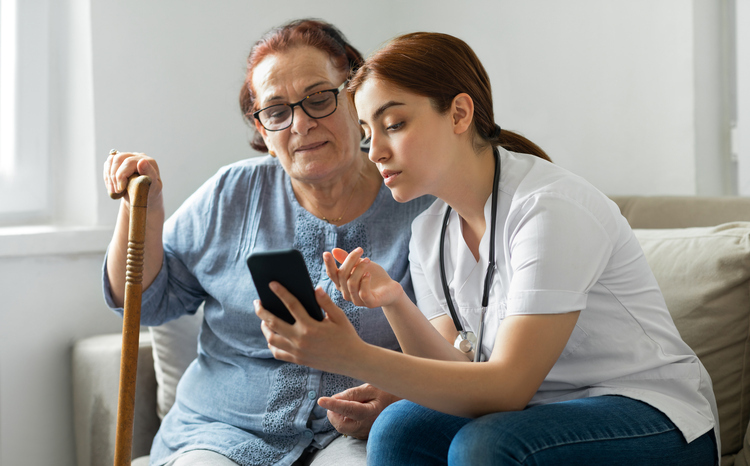 A young female carer helping an older woman with her mobile device